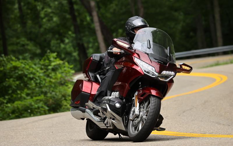 Motorcyclist in black gear riding a red motorcycle on a curving forest road.